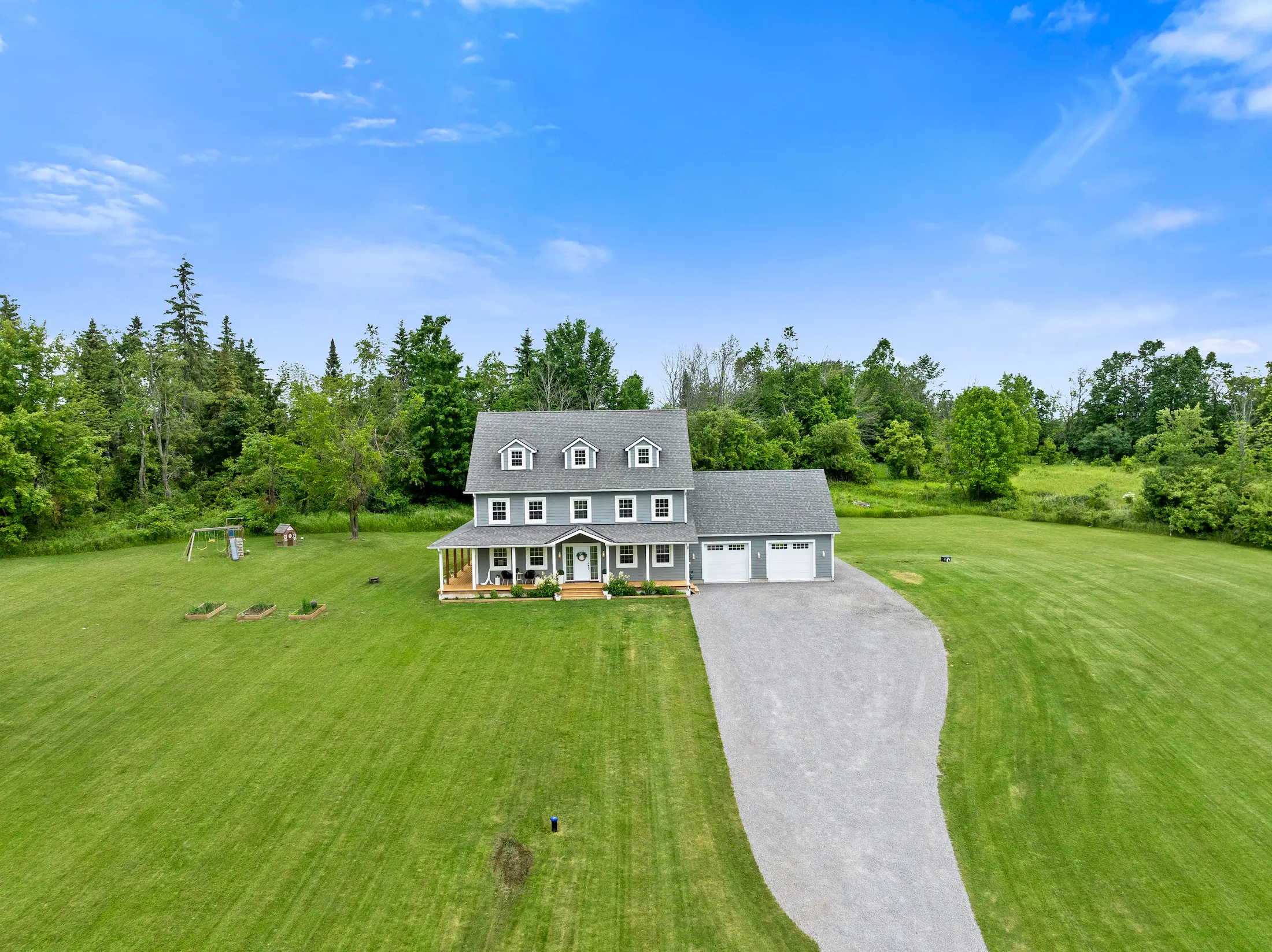 Aerial drone photography of a luxury custom home in Selwyn, Ontario, featuring a long gravel driveway and expansive green lawns.