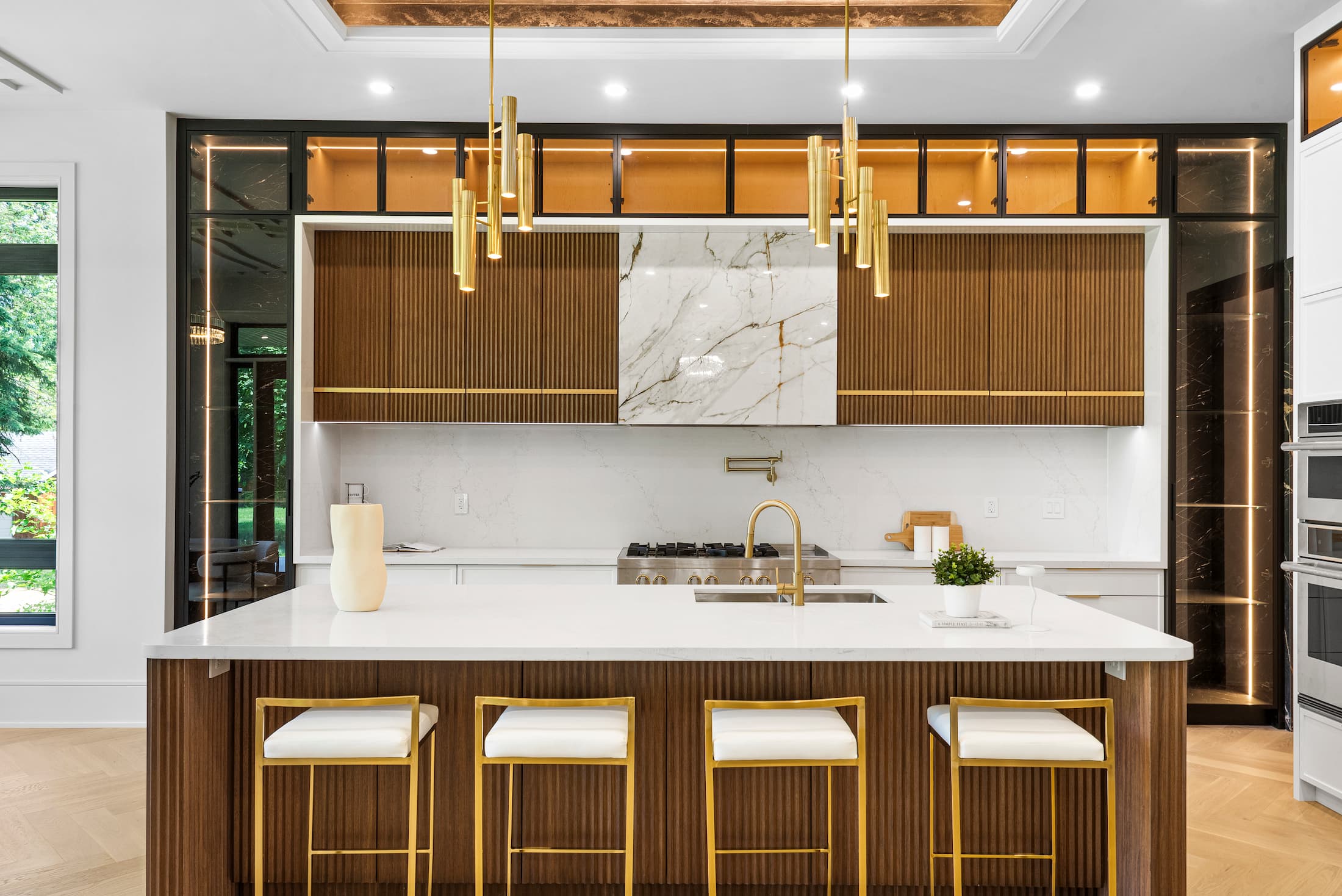 Modern luxury kitchen in a Pickering home featuring fluted wood cabinetry, brass pendant lighting, and a white marble backsplash.